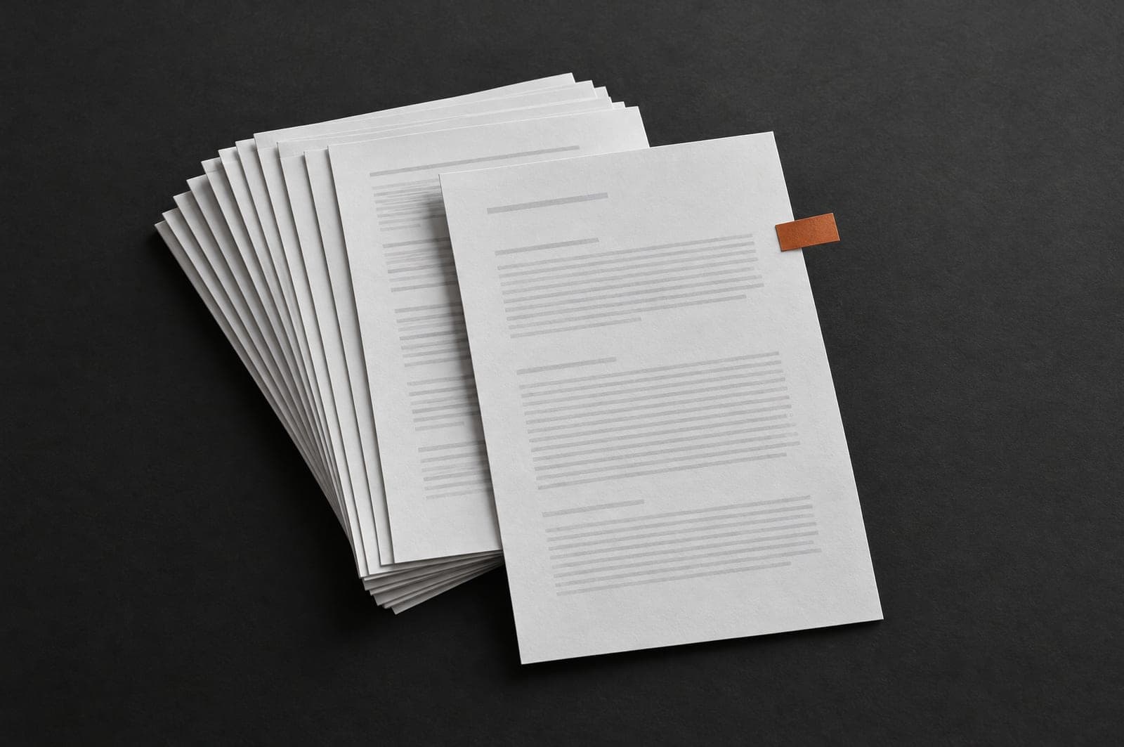 A fanned stack of identical printed pages on a dark surface, one marked with an orange tab